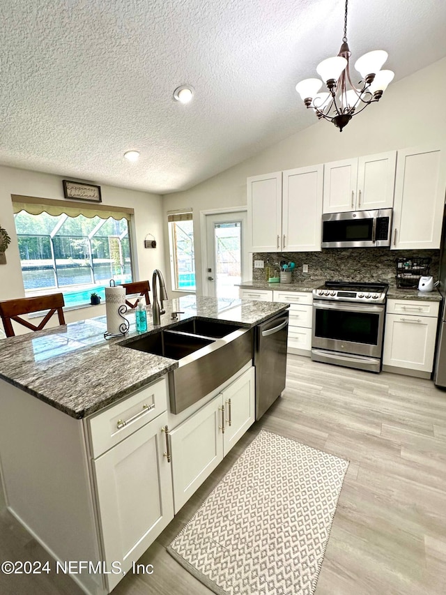 kitchen with stainless steel appliances, backsplash, white cabinets, vaulted ceiling, and a sink