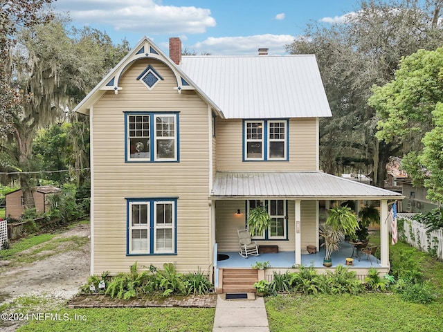 view of front of home with covered porch, metal roof, a chimney, and fence