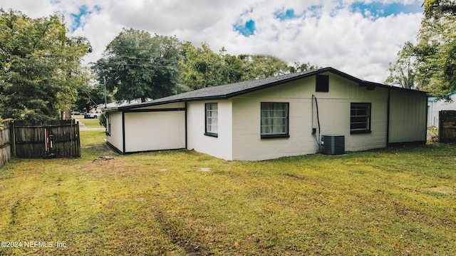 back of property featuring central AC unit, a lawn, concrete block siding, and fence