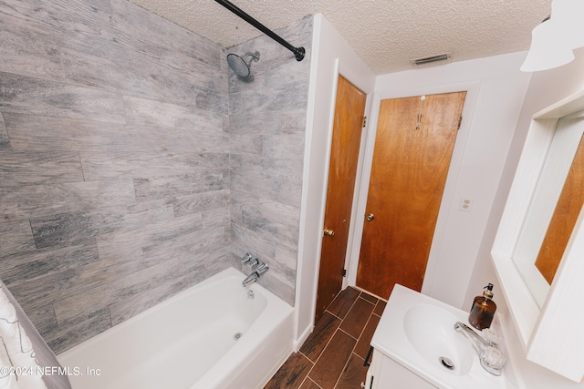 bathroom with tiled shower / bath combo, vanity, and a textured ceiling