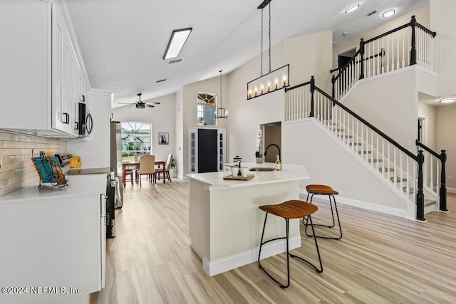 kitchen with backsplash, decorative light fixtures, stainless steel appliances, light hardwood / wood-style floors, and a kitchen breakfast bar