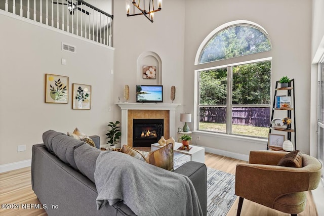 living room with a fireplace, a towering ceiling, light hardwood / wood-style flooring, and an inviting chandelier