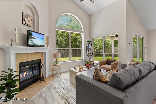 living room with a wealth of natural light, high vaulted ceiling, a tiled fireplace, and light wood-type flooring