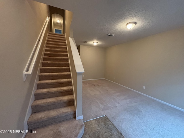 stairs with visible vents, a textured ceiling, carpet flooring, tile patterned flooring, and baseboards