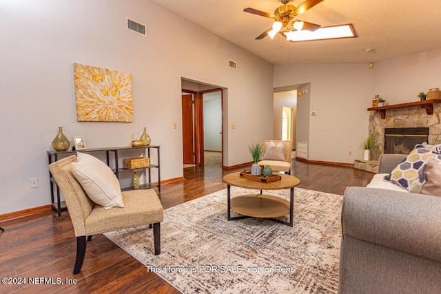 living room featuring dark hardwood / wood-style floors, vaulted ceiling, ceiling fan, and a stone fireplace