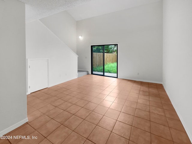 unfurnished room with a textured ceiling, light tile patterned floors, and high vaulted ceiling