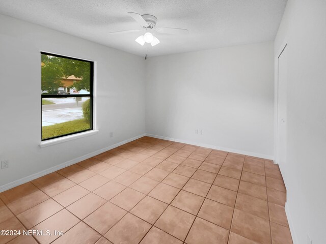 spare room with a textured ceiling, light tile patterned floors, and ceiling fan