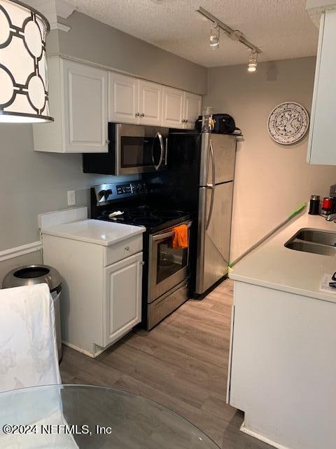 kitchen featuring a textured ceiling, hardwood / wood-style floors, appliances with stainless steel finishes, sink, and white cabinetry