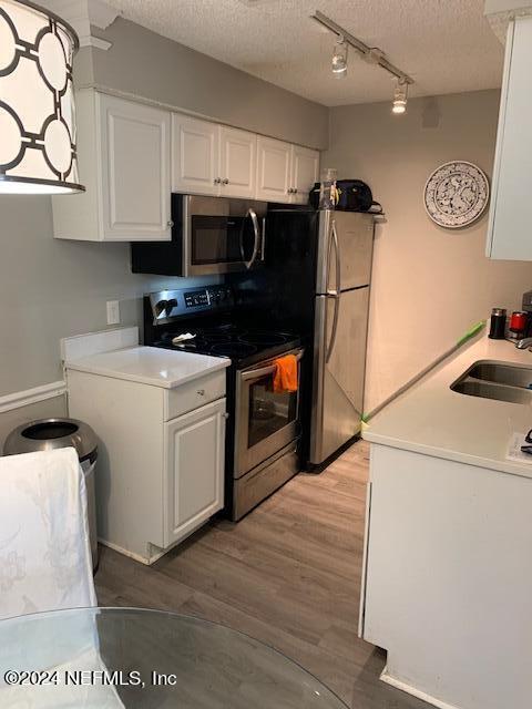 kitchen featuring light wood-type flooring, stainless steel appliances, white cabinets, a textured ceiling, and a sink