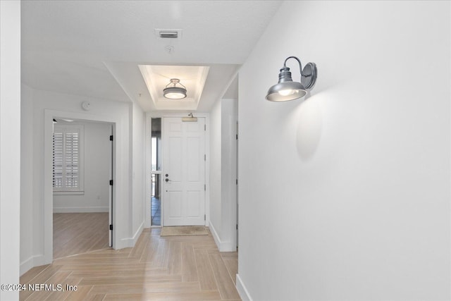 hallway with a textured ceiling, a raised ceiling, and light parquet flooring