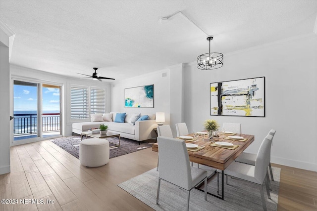 dining space with ceiling fan with notable chandelier, light wood-type flooring, and a textured ceiling