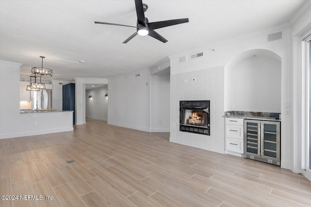 unfurnished living room with light wood-type flooring, ceiling fan with notable chandelier, a fireplace, and beverage cooler