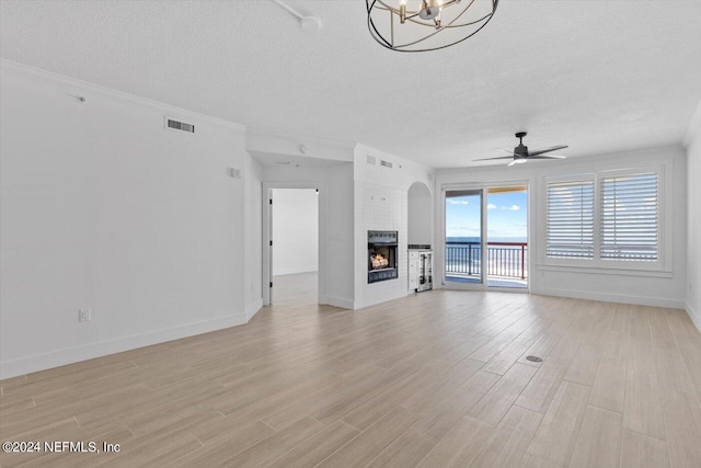 unfurnished living room with a textured ceiling, ceiling fan with notable chandelier, a large fireplace, and light hardwood / wood-style flooring