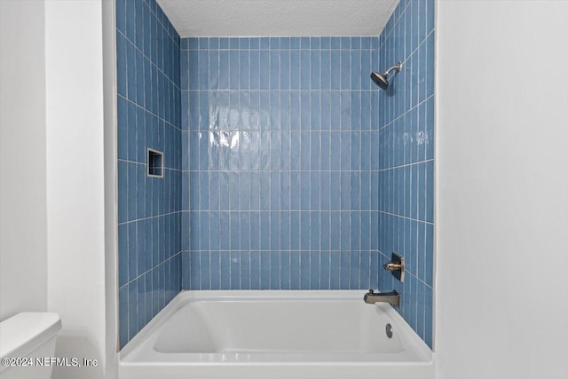 bathroom with a textured ceiling, tiled shower / bath, and toilet