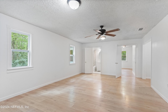 empty room featuring ceiling fan, a textured ceiling, plenty of natural light, and light hardwood / wood-style floors