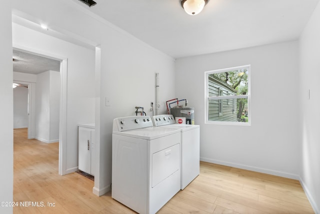 laundry area with washing machine and clothes dryer, water heater, and light hardwood / wood-style floors