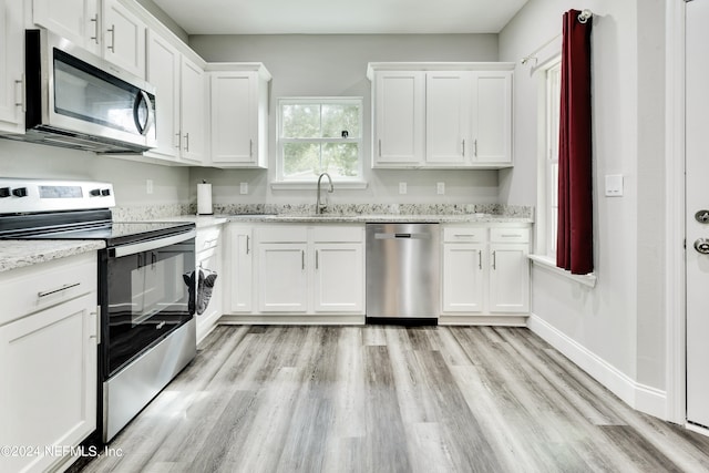 kitchen featuring light wood-type flooring, stainless steel appliances, sink, light stone countertops, and white cabinets