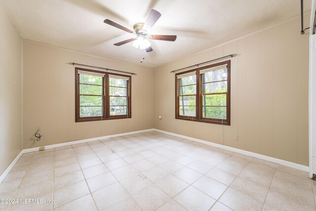 tiled empty room with ceiling fan, plenty of natural light, and ornamental molding