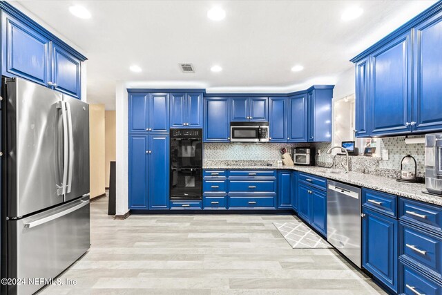 kitchen with stainless steel appliances, light wood-type flooring, blue cabinetry, light stone counters, and tasteful backsplash