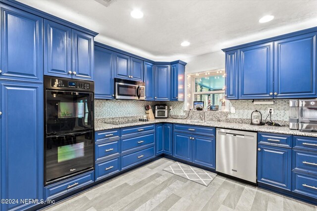 kitchen with light hardwood / wood-style flooring, black appliances, blue cabinetry, light stone counters, and tasteful backsplash