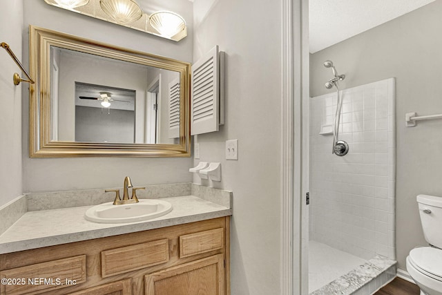 bathroom with ceiling fan, tiled shower, vanity, and toilet