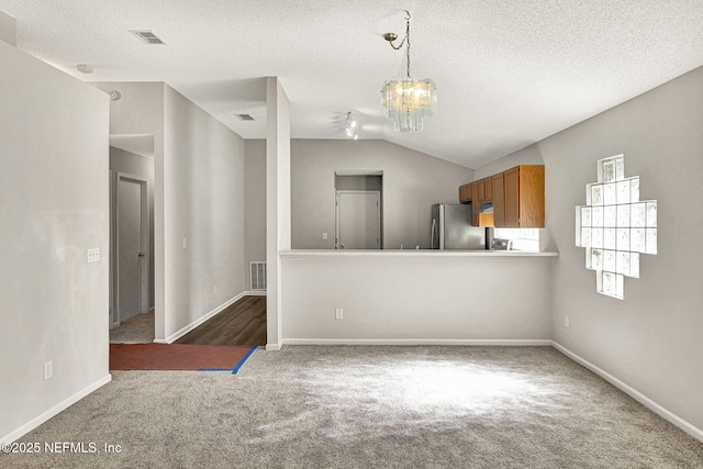 carpeted spare room with an inviting chandelier, vaulted ceiling, and a textured ceiling