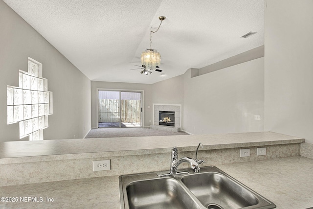 kitchen featuring sink, a tile fireplace, hanging light fixtures, a textured ceiling, and a chandelier