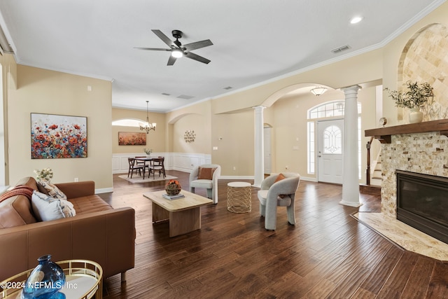 living room with dark wood-type flooring, a fireplace, decorative columns, ceiling fan with notable chandelier, and crown molding