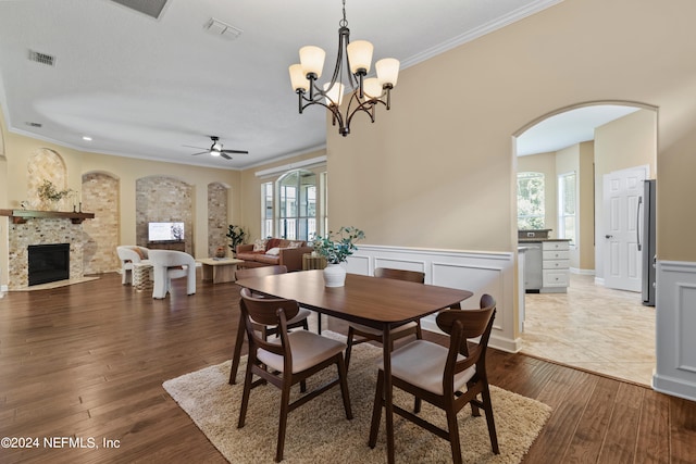 dining room with ceiling fan with notable chandelier, a tiled fireplace, plenty of natural light, and hardwood / wood-style floors