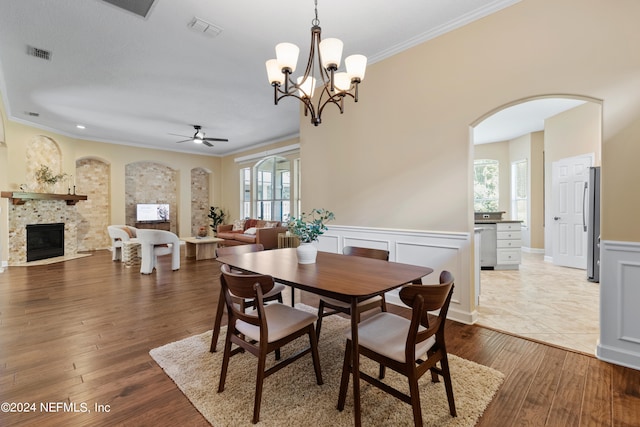 dining space featuring a wealth of natural light, ceiling fan with notable chandelier, light hardwood / wood-style floors, and a tile fireplace