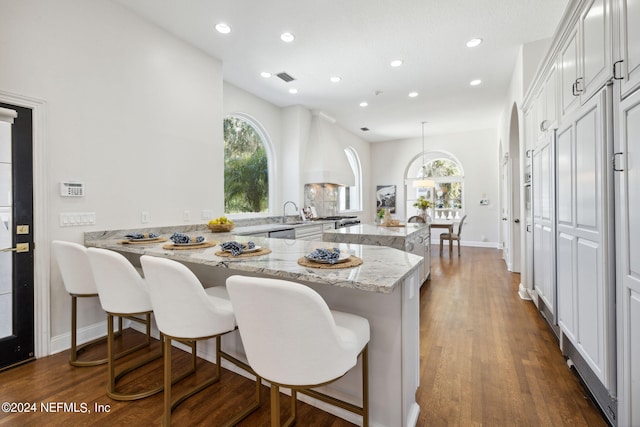 kitchen with light stone counters, kitchen peninsula, decorative light fixtures, a breakfast bar, and dark hardwood / wood-style flooring