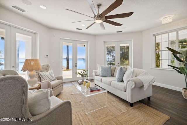 living room featuring a wealth of natural light, a water view, ceiling fan, and french doors