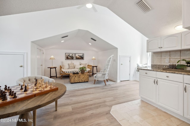 interior space with light hardwood / wood-style floors, vaulted ceiling, white cabinets, a textured ceiling, and ceiling fan