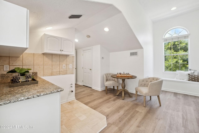 kitchen featuring white cabinets, lofted ceiling, light hardwood / wood-style floors, and light stone countertops