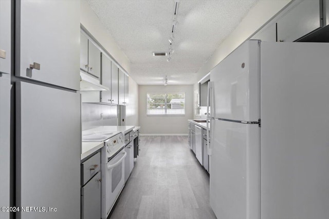 kitchen with a textured ceiling, under cabinet range hood, white appliances, visible vents, and light countertops