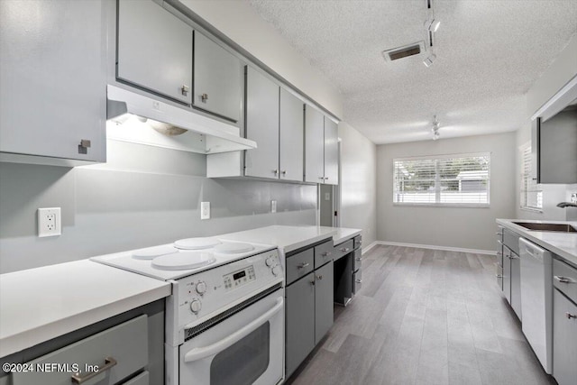 kitchen featuring white appliances, light hardwood / wood-style floors, a textured ceiling, and sink