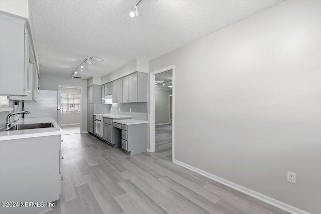 kitchen featuring a textured ceiling, a sink, light wood-style floors, light countertops, and freestanding refrigerator