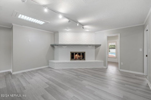 unfurnished living room with rail lighting, a textured ceiling, a brick fireplace, ornamental molding, and light hardwood / wood-style floors