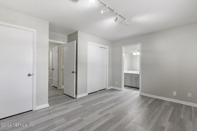 unfurnished bedroom featuring connected bathroom, rail lighting, and light hardwood / wood-style floors