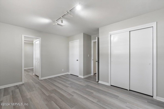 unfurnished bedroom featuring light hardwood / wood-style floors, a closet, and track lighting