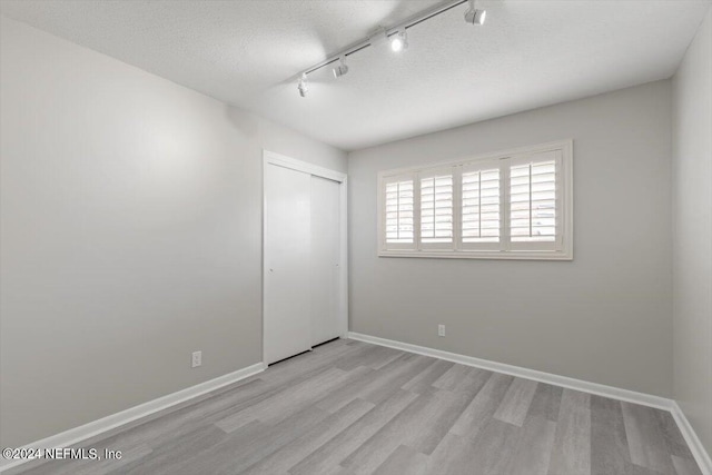 empty room with light hardwood / wood-style flooring, a textured ceiling, and rail lighting