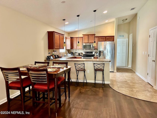 kitchen with a kitchen breakfast bar, kitchen peninsula, stainless steel appliances, sink, and decorative light fixtures