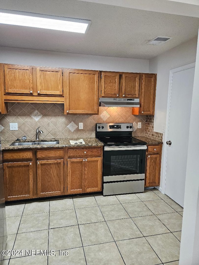 kitchen featuring dark stone counters, tasteful backsplash, stainless steel range with electric cooktop, light tile patterned floors, and sink