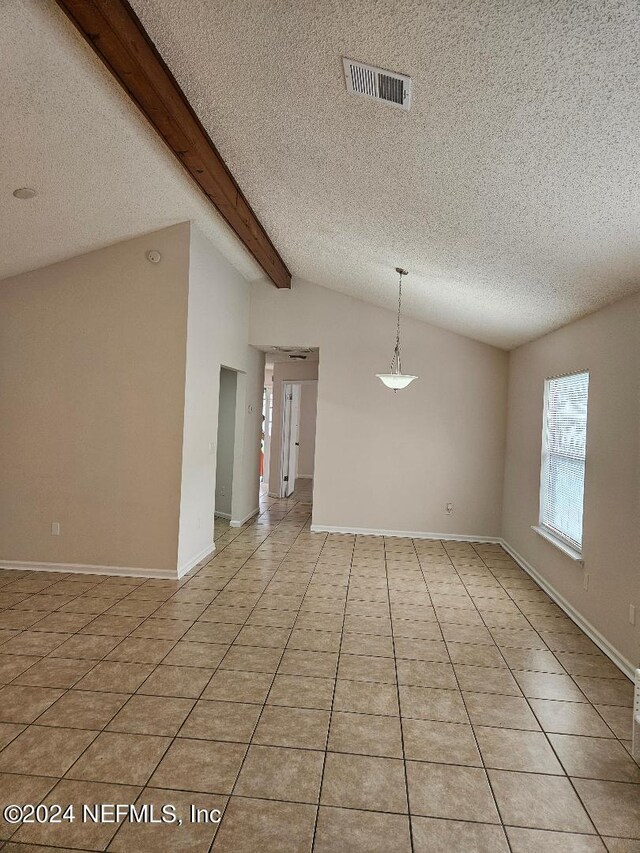 empty room with light tile patterned floors, lofted ceiling with beams, and a textured ceiling