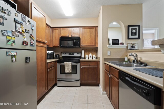 kitchen with a textured ceiling, sink, light tile patterned floors, and appliances with stainless steel finishes