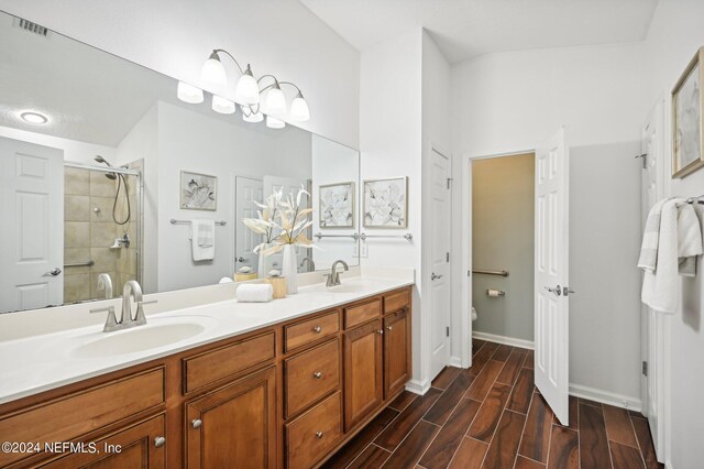 bathroom with hardwood / wood-style flooring, vaulted ceiling, a shower with shower door, vanity, and toilet