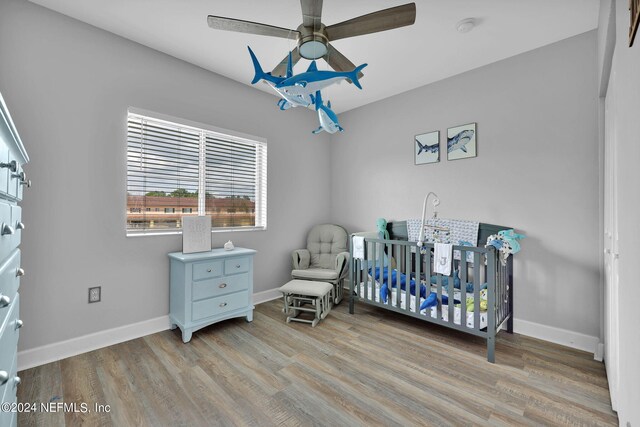 bedroom featuring a nursery area, wood-type flooring, and ceiling fan