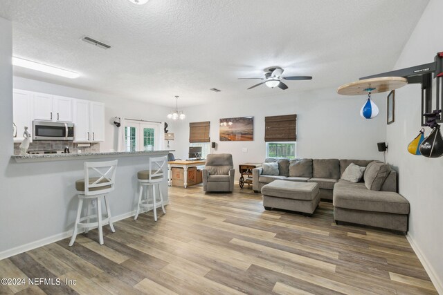 living room featuring ceiling fan with notable chandelier, a wealth of natural light, light hardwood / wood-style floors, and a textured ceiling