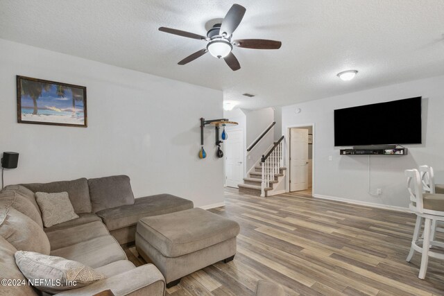 living room featuring wood-type flooring, ceiling fan, and a textured ceiling