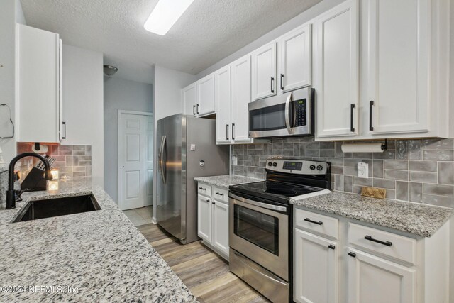 kitchen with appliances with stainless steel finishes, light hardwood / wood-style floors, white cabinetry, light stone countertops, and sink